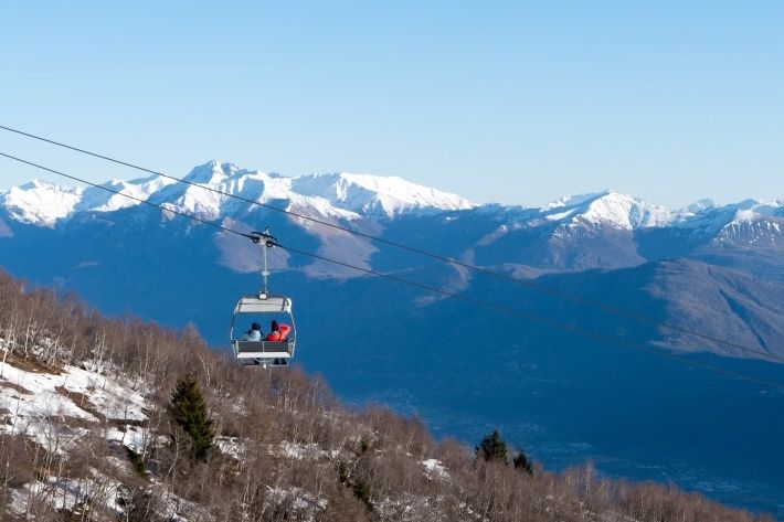 Zwei Personen in einer Seilbahn mit fanatstischem Ausblick Richtung schneebedeckter Berge.