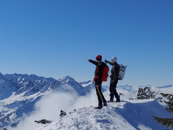 Zwei Personen auf einem schneebedeckten Gipfel zeigen in die gleiche Richtung
