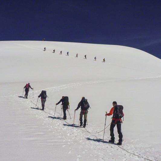 Zwei große Seilschaften laufen im Zickzack auf einen schneebedeckten Gipfel